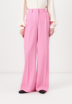 Persoon die hoge roze wijde broek draagt, gecombineerd met een witte blouse met lange mouwen en zwarte schoenen.