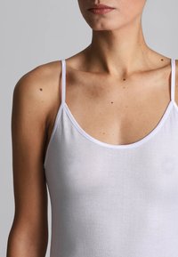 Camisola bianca con spalline sottili, realizzata in un tessuto leggero e morbido, con scollatura rotonda che lascia intraveder la tonalità della pelle sottostante.