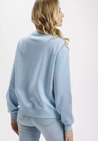 Jasnoniebieski bawełniany sweter z luźnym krojem. Posiada ściągacze w mankietach i u dołu, widoczne szwy oraz okrągły dekolt.