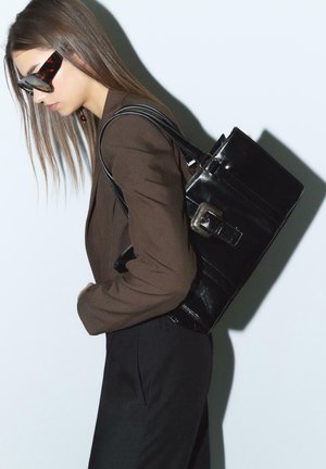 Borsa a tracolla nera lucida con design strutturato, caratterizzata da un dettaglio in metallo argentato e due manici, su uno sfondo neutro.