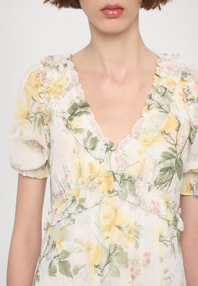 Bloemjurkje met een gerimpelde rand, korte pofmouwen en een v-hals. Kleuren zijn geel, groen en roze op een lichte achtergrond.