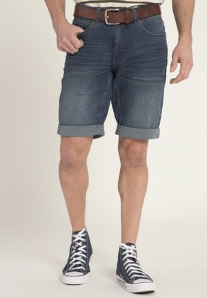 Shorts en denim avec un délavé foncé, ourlets retroussés et design à cinq poches. Portés avec une ceinture marron et des baskets montantes bleu marine.