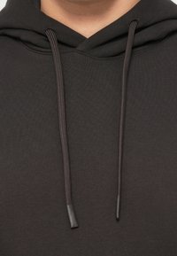 Gros plan d'une personne portant un sweat à capuche gris foncé avec des cordons visibles suspendus à la capuche.