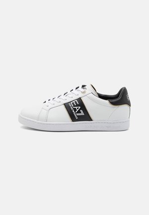 Zapatilla baja blanca con detalles en negro, cordones y logo EA7 Emporio Armani en el costado y talón, presentada sobre un fondo blanco.