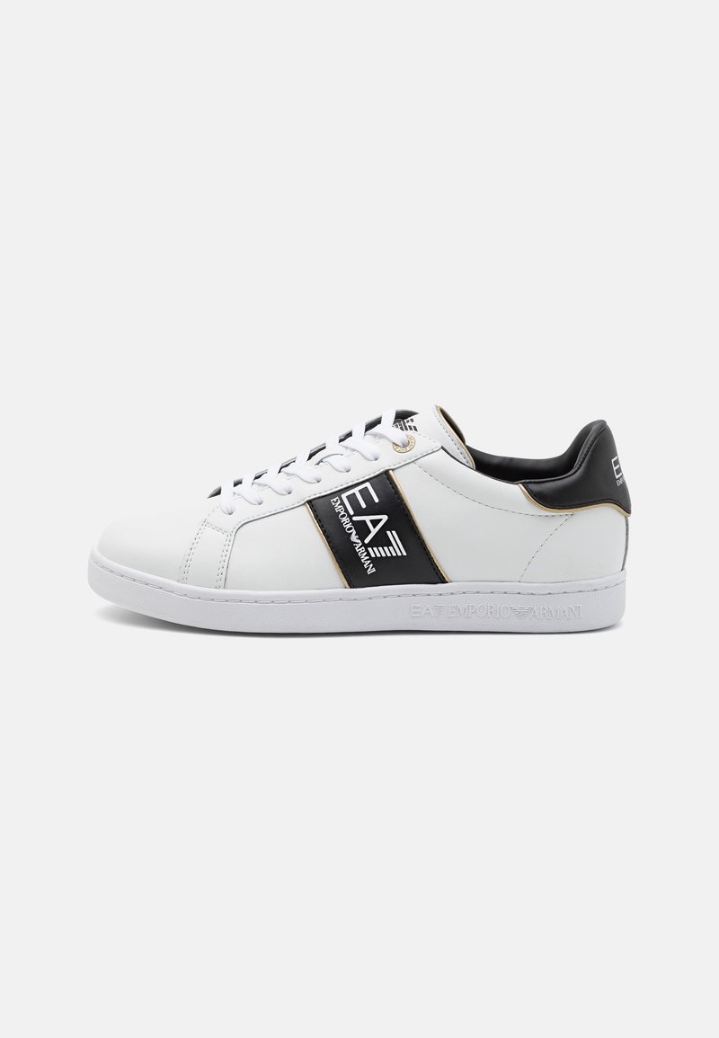 Baskets basses blanches avec des accents noirs, des lacets et le logo EA7 Emporio Armani sur le côté et le talon, présentées sur un fond blanc.