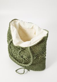 Groene geweven tas van textuurmateriaal, met een crèmekleurige binnenkant en een klein binnenzakje. De tas heeft striksluitingen.