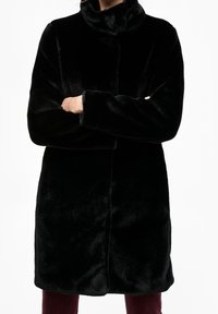 Sort kunstpelsjakke med høj krave, lange ærmer og lige snit, der har en blød tekstur og ingen synlige lukninger.