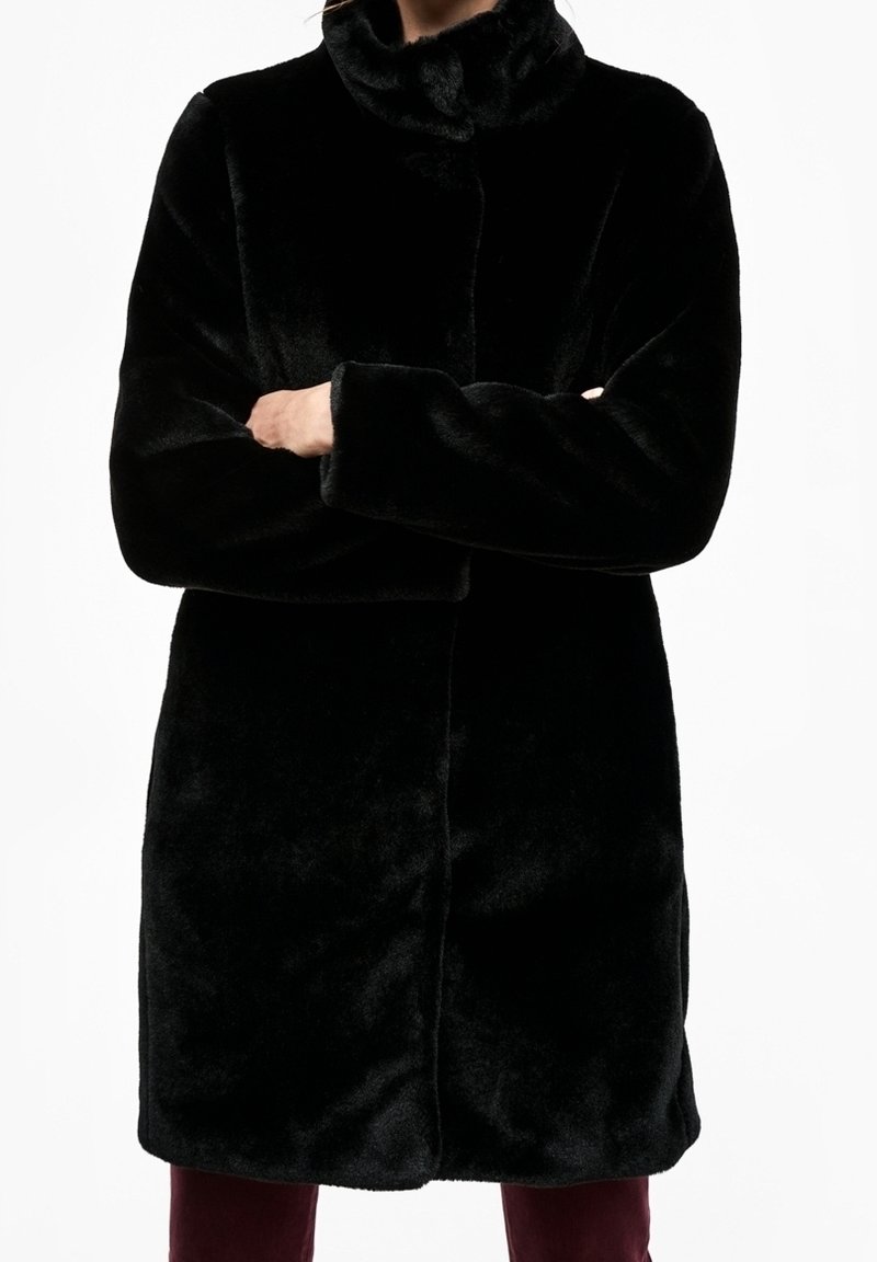 Sort kunstpelsjakke med høj krave, lange ærmer og lige snit, der har en blød tekstur og ingen synlige lukninger.