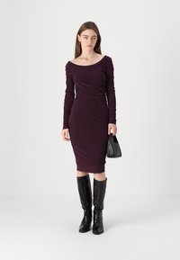 Long-sleeve, burgundy dress with a boat neckline, featuring a fitted silhouette and gathered detailing. Paired with knee-high black boots and a handbag.