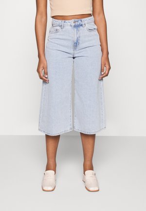 Culottes de ganga de lavagem clara com perna reta e bainha desfiada. O design de cintura alta possui bolsos frontais e fecho de botão. Usados com sapatos claros.