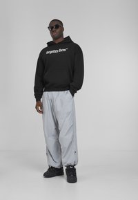 Black hoodie with "forgotten faces" graphic, gray lightweight pants, and black sneakers; individual wearing dark sunglasses.