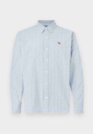 Ανοιχτό μπλε και άσπρο ριγέ πουκάμισο μακρυμάνικο με γιακά με κουμπιά, διακοσμημένο με μια μικρή καφέ κεντημένη φιγούρα ζώου στο στήθος.