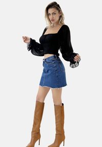 Top nero aderente con scollatura quadrata e maniche a sbuffo abbinato a una mini gonna di jeans sfrangiata e stivali con tacco alti fino al ginocchio di colore marrone.