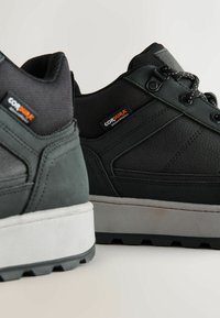 Musta kengät, jotka on valmistettu kestävästä materiaalista. Ominaisuuksiin kuuluvat tekstuuripinta, vahvistetut korostukset, kontrastivärinen harmaa pohja ja sävy säikeet.