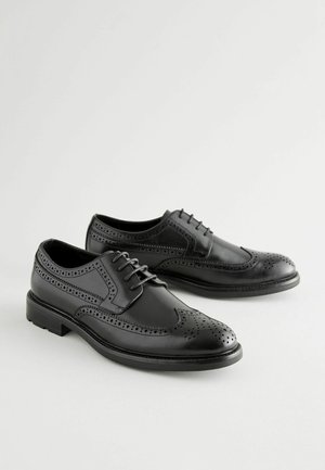 Melnā ādas brogue kurpes ar dekoratīvām perforācijām, saistīšanas dizains, noapaļota purngala forma un plakana gumijas zole.