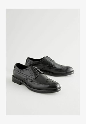 Crne kožne brogue cipele s dekorativnim perforacijama, vezanjem, okruglim vrhom i ravnim gumenim potplatom.