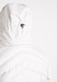 Vue arrière d'une veste matelassée blanche avec une capuche réglable dotée d'un cordon rouge et d'un fermoir noir.