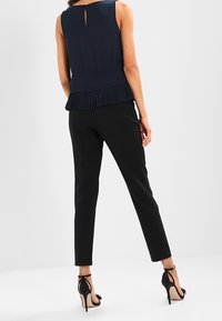 Marinblå ärmlös topp med plisserad nederkant och nyckelhål bak, i kombination med figursydda svarta byxor och svarta klackar med remmar prydda med blommor.