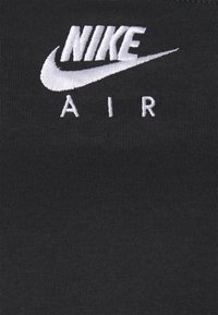 Tissu noir avec le logo Nike en broderie blanche, accompagné de "AIR" en dessous, sur une surface lisse et côtelée.