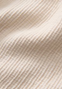 Tessuto in un colore beige chiaro con un pattern ondulato e texturizzato. Il materiale è morbido, con una leggera lucentezza e linee sottili.
