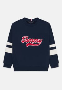 Mörkblå sweatshirt med en vit och röd broderad "Tommy"-logotyp. Har vita ränder på ärmarna samt ribbade mudd och krage.