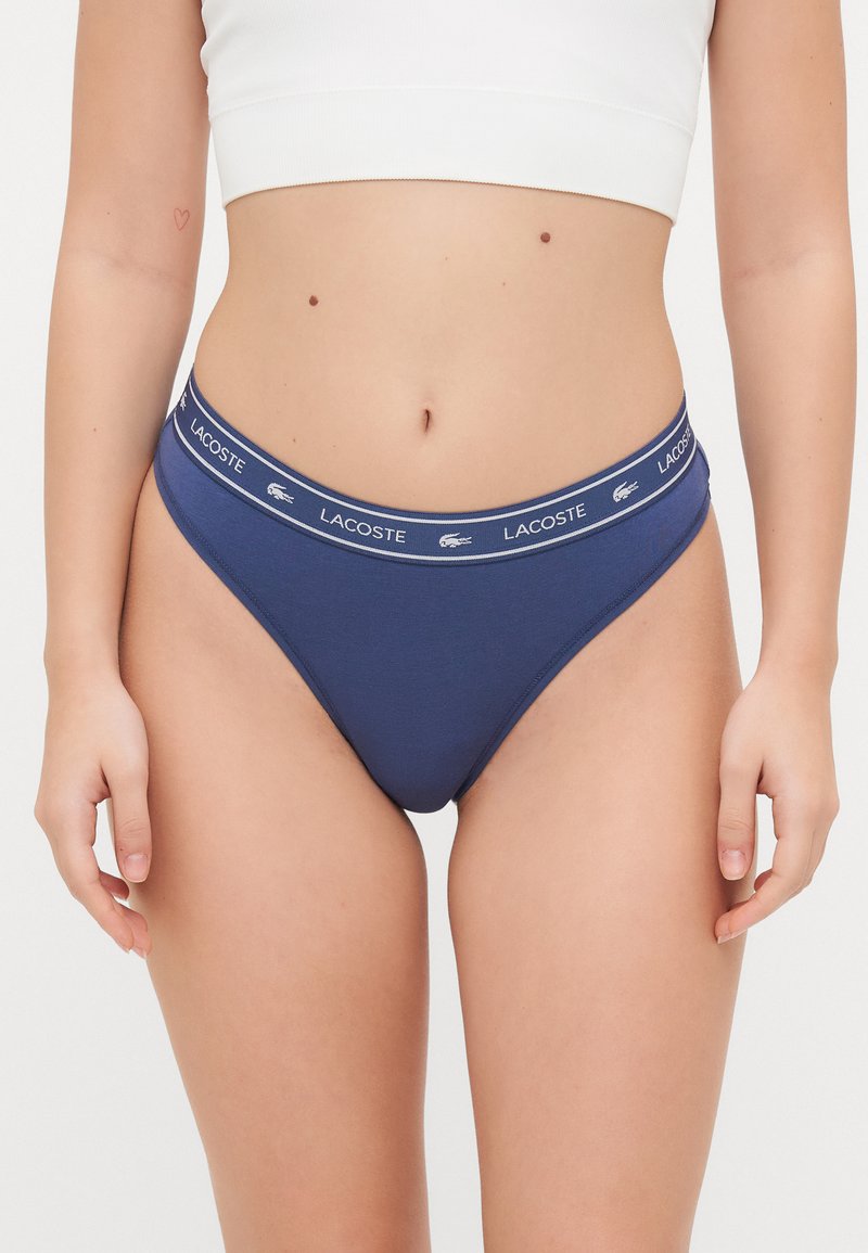 Granatowe bawełniane figi hipster z kontrastującą tasiemką w pasie, na której znajduje się białe logo Lacoste. Gładka tekstura i dopasowany krój.