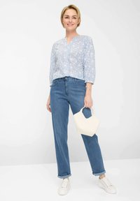 Light blue patterned blouse with long sleeves, paired with straight-leg dark blue denim jeans. Holding a small white handbag, wearing white sneakers.