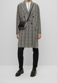 Dvousetový kostkovaný kabát v šedé barvě, s texturou houndstooth, kombinovaný s černými kalhotami a mokasíny. Obsahuje malou černou kabelku na rameno.