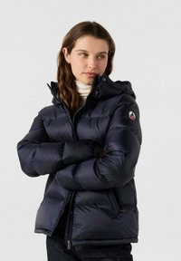 Chaqueta acolchada azul marino con capucha, diseño acolchado, cremallera frontal, puños elásticos y detalle de logo en la manga. Material suave y brillante.