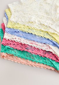 Stack of multicolored lace fabric pieces with scalloped edges in white, yellow, blue, pink, green, and peach tones on a light surface.