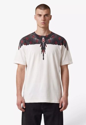 Giovane uomo che indossa una maglietta bianca con un design dettagliato di ali di uccello nere e rosse sulle spalle e sul petto.