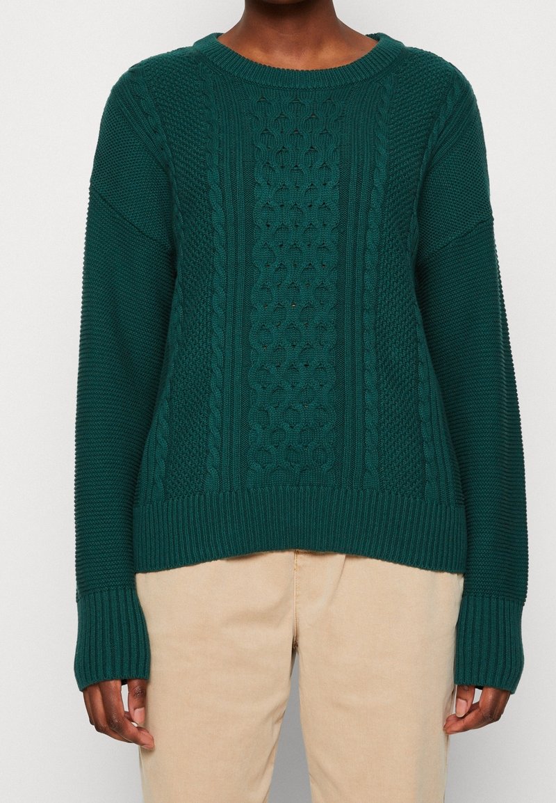 Pull en tricot bleu sarcelle avec un panneau central texturé, des poignets et un ourlet côtelés. Le tissu présente un mélange de motifs torsadés et de points.