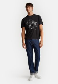 Černé bavlněné tričko s bílým grafickým designem s rokem "1965." V kombinaci s modrými džíny a bílými teniskami.