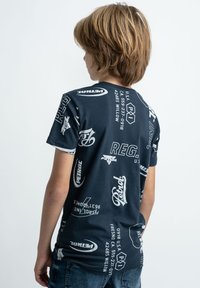 Námořnické modré bavlněné tričko s různými bílými logy a textovými designy. Krátké rukávy, kulatý výstřih a volný střih. Zobrazeno z hlediska zad.