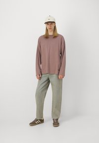 Langermet skjorte i støvete rosa, lyse denim bukser, brune joggesko med hvite og gule striper, kremfarget caps med mørk skjerm og logo.