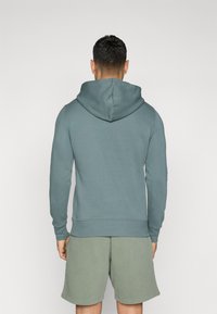 Felpa con cappuccio in morbido tessuto verde acqua chiaro, con vestibilità comoda, dotata di tasca a marsupio e polsini a costine, abbinata a pantaloni corti verde oliva.