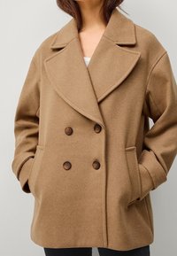 Bruine wolmix dubbelzijdige jas met grote revers, twee voorkzakken en donkere knopen, met een ontspannen pasvorm en zachte textuur.