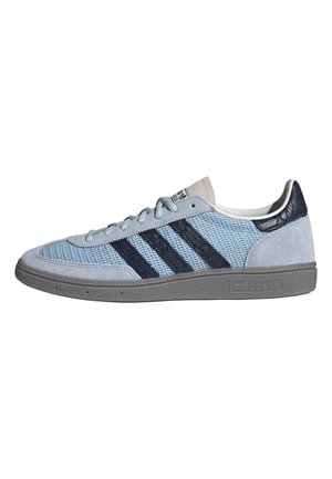Zapatilla Adidas azul claro con rayas azul oscuro, puntera y talón de ante, suela texturizada y cierre de cordones, vista lateral sobre fondo blanco.