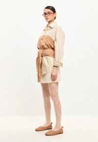 Camisa a rayas beige, con un suéter color caqui atado a la cintura. Falda de color claro y medias estampadas, combinadas con bailarinas marrones.