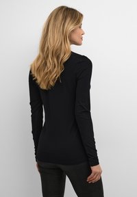 Črna dolga majica z dolgimi rokavi, prilegajočega kroja, gladke teksture in okroglim izrezom, kombinirana z vzorčenimi pajkicami, prikazana s hrbtne strani.