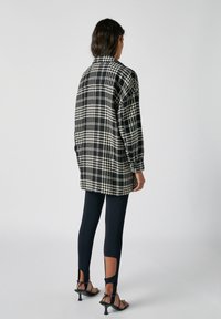 Czarno-biała, w kratkę, oversize'owa kurtka z kołnierzem, połączona z czarnymi legginsami z wcięciami przy kostkach i sandałkami na obcasie.