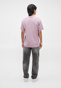 T-shirt viola chiaro a maniche corte con vestibilità rilassata, abbinato a jeans grigi a gamba larga e testurizzati e scarpe da ginnastica bianche. Design minimale.