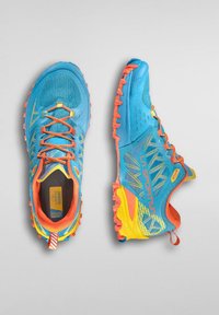 Běžecké boty do terénu s modrou síťovinou, oranžovými detaily, žlutou patou a agresivní podrážkou s víc směrovými výstupky pro lepší grip.