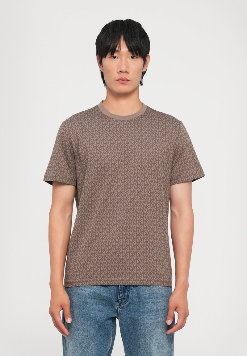 Brown short-sleeve t-shirt with a repeating geometric pattern. Crew neck design and soft texture, paired with blue jeans.