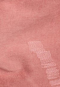 Tela roja con una textura suave y un tejido diagonal. Presenta una zona desgastada que crea un contraste con el color circundante.