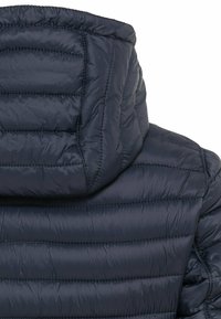 Marinekleurige pufferjack met een hoge kraag, geborduurde textuur en een zachte, glanzende afwerking. Zichtbare stikseldetails versterken de structuur.