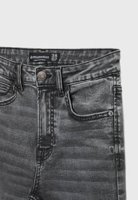 Jeans de denim negros de cintura alta con un acabado desgastado, detalles en los bolsillos frontales y un cierre de botón metálico. La etiqueta muestra la talla 38.