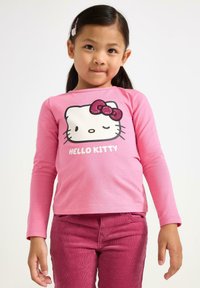 T-shirt a maniche lunghe rosa con design di Hello Kitty in bianco e nero e un fiocco rosa luccicante. Abbinato a pantaloni in corduroy rosa.