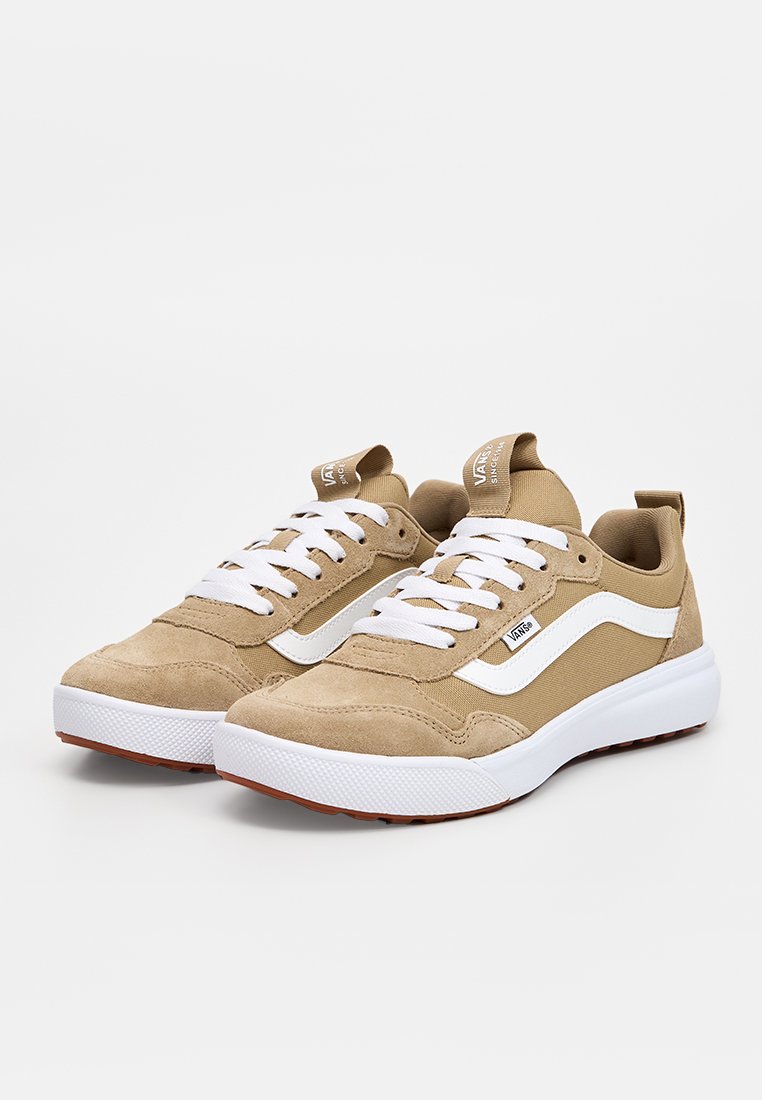 Zapatillas beige con parte superior de ante y lona, cordones blancos, una franja lateral blanca y suela de goma texturizada con acentos marrones.