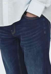 Jeans blu scuro in denim, con un design a gamba dritta e cuciture visibili in giallo. Le tasche sono accessibili e funzionali.